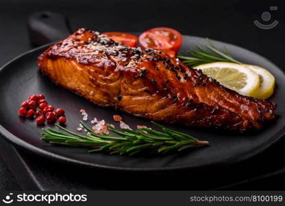 Delicious grilled red salmon fish with sauce, sesame seeds, spices and herbs on a dark concrete background