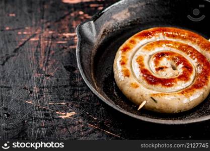 Delicious grilled sausage in a frying pan. Against a dark background. High quality photo. Delicious grilled sausage in a frying pan.