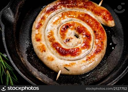 Delicious grilled sausage in a frying pan. Against a dark background. High quality photo. Delicious grilled sausage in a frying pan.