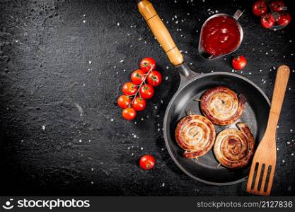 Delicious grilled sausages in a frying pan with fresh tomatoes. On a black background. High quality photo. Delicious grilled sausages in a frying pan with fresh tomatoes.
