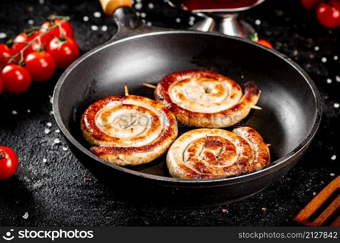 Delicious grilled sausages in a frying pan with fresh tomatoes. On a black background. High quality photo. Delicious grilled sausages in a frying pan with fresh tomatoes.