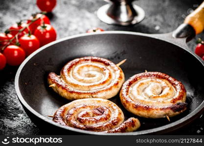 Delicious grilled sausages in a frying pan with fresh tomatoes. On a black background. High quality photo. Delicious grilled sausages in a frying pan with fresh tomatoes.