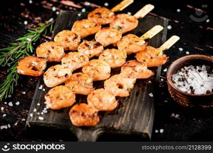 Delicious grilled shrimp on a cutting board with rosemary and spices. On a rustic dark background. High quality photo. Delicious grilled shrimp on a cutting board with rosemary and spices.