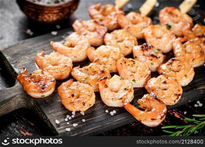 Delicious grilled shrimp on a cutting board with rosemary and spices. On a rustic dark background. High quality photo. Delicious grilled shrimp on a cutting board with rosemary and spices.