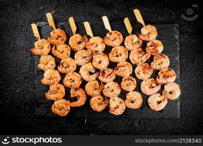 Delicious grilled shrimp on skewers on a stone board. On a black background. High quality photo. Delicious grilled shrimp on skewers on a stone board.