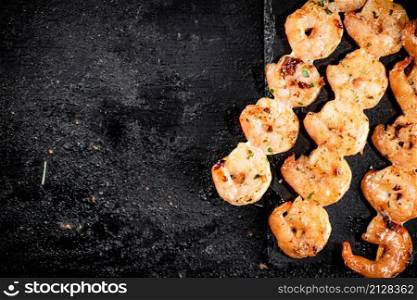 Delicious grilled shrimp on skewers on a stone board. On a black background. High quality photo. Delicious grilled shrimp on skewers on a stone board.