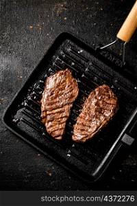 Delicious grilled steak in a frying pan. On a black background. High quality photo. Delicious grilled steak in a frying pan.