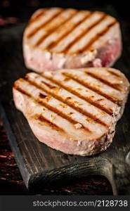 Delicious grilled tuna steak on a cutting board. On a rustic dark background. High quality photo. Delicious grilled tuna steak on a cutting board.