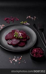 Delicious hea<hy boi≤d ruby-colored beets sliced   on a black plate on a dark concrete background