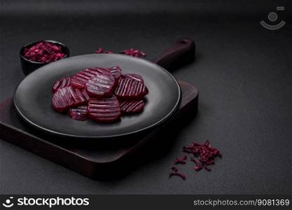 Delicious healthy boiled ruby-colored beets sliced   on a black plate on a dark concrete background