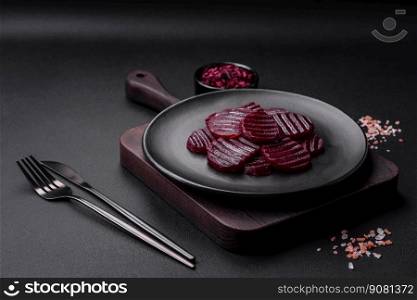Delicious healthy boiled ruby-colored beets sliced   on a black plate on a dark concrete background