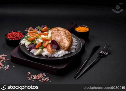 Delicious healthy breakfast consisting of chicken, rice, greens and cherry tomatoes on a black ceramic plate on a dark concrete background