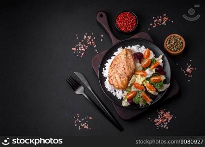 Delicious healthy breakfast consisting of chicken, rice, greens and cherry tomatoes on a black ceramic plate on a dark concrete background