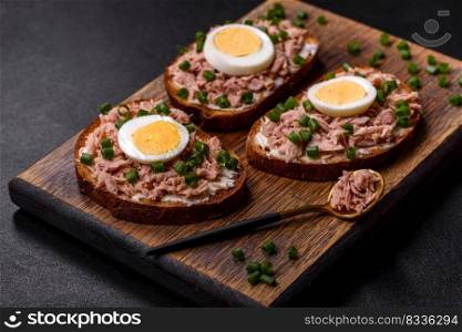 Delicious healthy sandwich with tuna, croutons, boiled egg, herbs and butter on a dark concrete background. Delicious healthy sandwich with tuna, croutons, boiled egg, herbs and butter