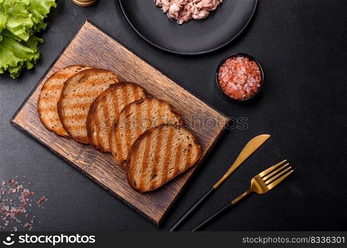 Delicious healthy sandwich with tuna, croutons, boiled egg, herbs and butter on a dark concrete background. Delicious healthy sandwich with tuna, croutons, boiled egg, herbs and butter