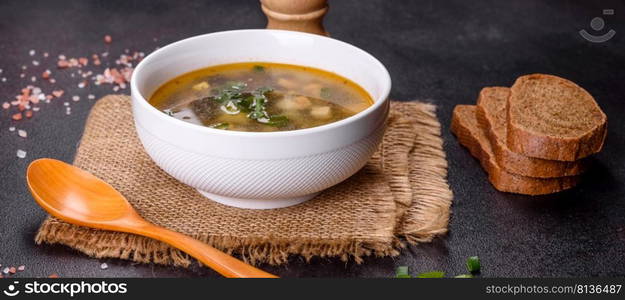 Delicious healthy soup with sorrel, tomato, potatoes, spices and herbs in a white bowl against a dark concrete background. Vegetarian dish. Delicious healthy soup with sorrel, tomato, potatoes, spices and herbs in a white bowl