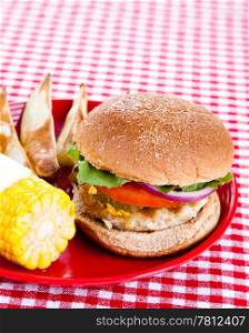 Delicious healthy turkey burger on a whole grain bun, with baked potato wedges and corn on the cob.