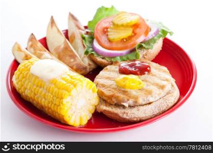 Delicious healthy turkey burger on a whole grain bun, with baked potato wedges and corn on the cob. Isolated on white background.