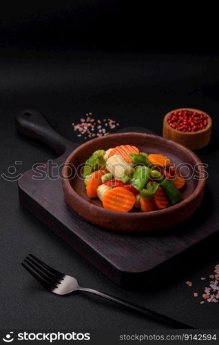 Delicious healthy vegetables steamed carrots, broccoli, asparagus beans and peppers on a dark concrete background