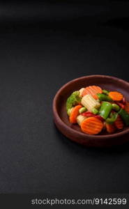 Delicious healthy vegetables steamed carrots, broccoli, asparagus beans and peppers on a dark concrete background