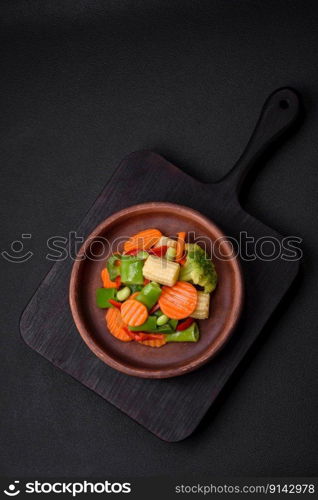 Delicious healthy vegetables steamed carrots, broccoli, asparagus beans and peppers on a dark concrete background