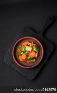 Delicious healthy vegetables steamed carrots, broccoli, asparagus beans and peppers on a dark concrete background