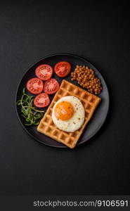 Delicious hearty breakfast consisting of a fried egg, Belgian waffle, lentils, microgreens with spices and herbs on a dark concrete background