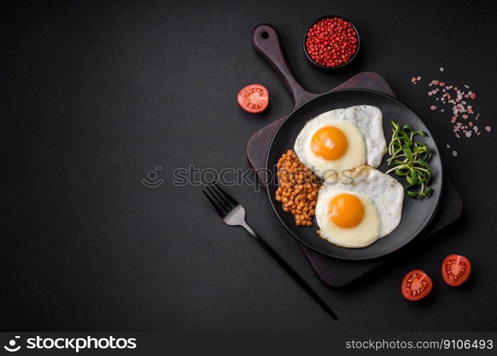 Delicious hearty breakfast consisting of two fried eggs, canned lentils, microgreens with spices and herbs on a dark concrete background