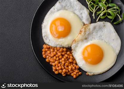 Delicious hearty breakfast consisting of two fried eggs, canned lentils, microgreens with spices and herbs on a dark concrete background