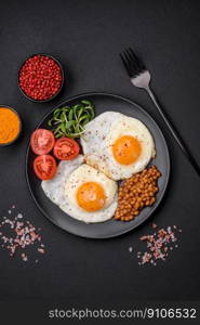 Delicious hearty breakfast consisting of two fried eggs, canned lentils, microgreens with spices and herbs on a dark concrete background