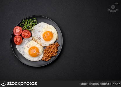 Delicious hearty breakfast consisting of two fried eggs, canned lentils, microgreens with spices and herbs on a dark concrete background