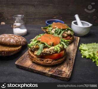 delicious homemade burgers with chicken in mustard sauce with arugula and herbs on a cutting board with lettuce and spices on wooden rustic background close up