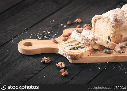 Delicious homemade dessert, a sliced pound cake filled with poppy seeds and nuts, displayed on a black wooden table, surrounded by roasted walnuts and almonds.