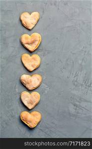 Delicious homemade gingerbread shortbread cookies in the shape of unpresentable hearts laid out vertically in a row on a gray concrete surface, image with copy space.. Delicious homemade ginger shortbread gingerbread cookie on a gray concrete surface.