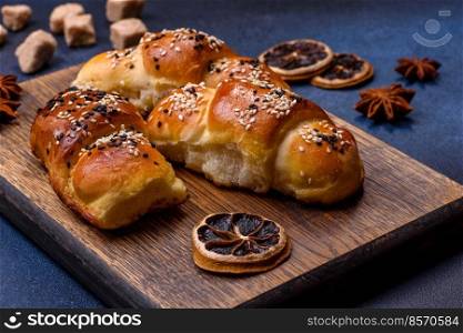 Delicious homemade pastries with apricot jam sprinkled with sesame seeds on a wooden cutting board against a blue concrete background. Delicious homemade pastries with apricot jam sprinkled with sesame seeds