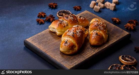 Delicious homemade pastries with apricot jam sprinkled with sesame seeds on a wooden cutting board against a blue concrete background. Delicious homemade pastries with apricot jam sprinkled with sesame seeds