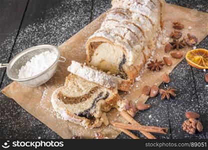 Delicious homemade pound cake on a baking paper, surrounded by roasted walnuts and almonds, covered in powdered sugar, on a black wooden table.