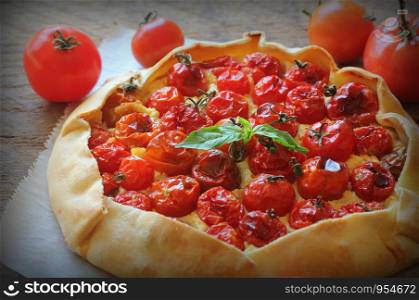 Delicious homemade rustic open pie or galette with tomato, cheese on wooden background. Top view .. Delicious homemade rustic open pie or galette with tomato, cheese on wooden background. Top view