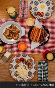 Delicious homemade style breakfast with crispy bacon, eggs, french toast, sausage, grilled tomatoes and orange juice. Top view shot