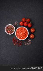 Delicious hot spicy red sauce with salt and spices in a ceramic bowl on a dark concrete background