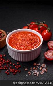 Delicious hot spicy red sauce with salt and spices in a ceramic bowl on a dark concrete background