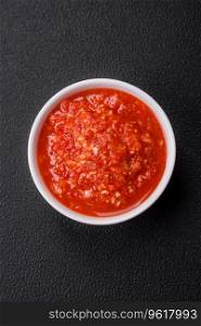 Delicious hot spicy red sauce with salt and spices in a ceramic bowl on a dark concrete background