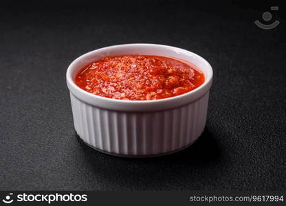 Delicious hot spicy red sauce with salt and spices in a ceramic bowl on a dark concrete background