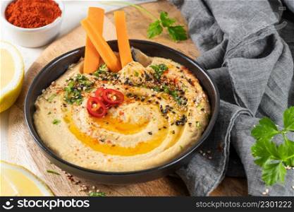 Delicious hummus in ceramic bow lwith carrot stick dipped in hummus. Colorful snack composition on a white background.
