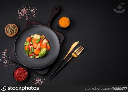 Delicious juicy broccoli vegetables, carrots, asparagus beans, bell peppers steamed in a black plate on a dark concrete background