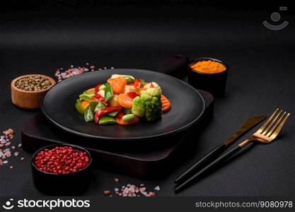 Delicious juicy broccoli vegetables, carrots, asparagus beans, bell peppers steamed in a black plate on a dark concrete background