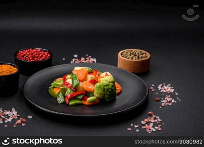 Delicious juicy broccoli vegetables, carrots, asparagus beans, bell peppers steamed in a black plate on a dark concrete background