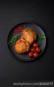 Delicious juicy chicken thighs baked with salt, spices and herbs in a ceramic plate on a dark concrete background