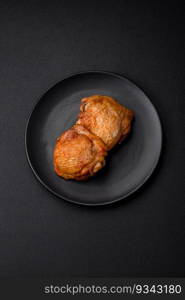 Delicious juicy chicken thighs baked with salt, spices and herbs in a ceramic plate on a dark concrete background