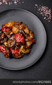 Delicious juicy fresh salad of baked eggplant, tomatoes, sweet peppers, sesame seeds, spices and salt on a dark concrete background